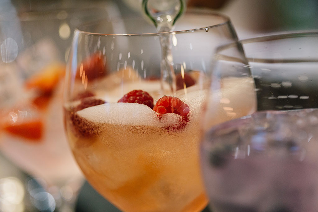 Lemonade being poured into a gin glass with gin and raspberries